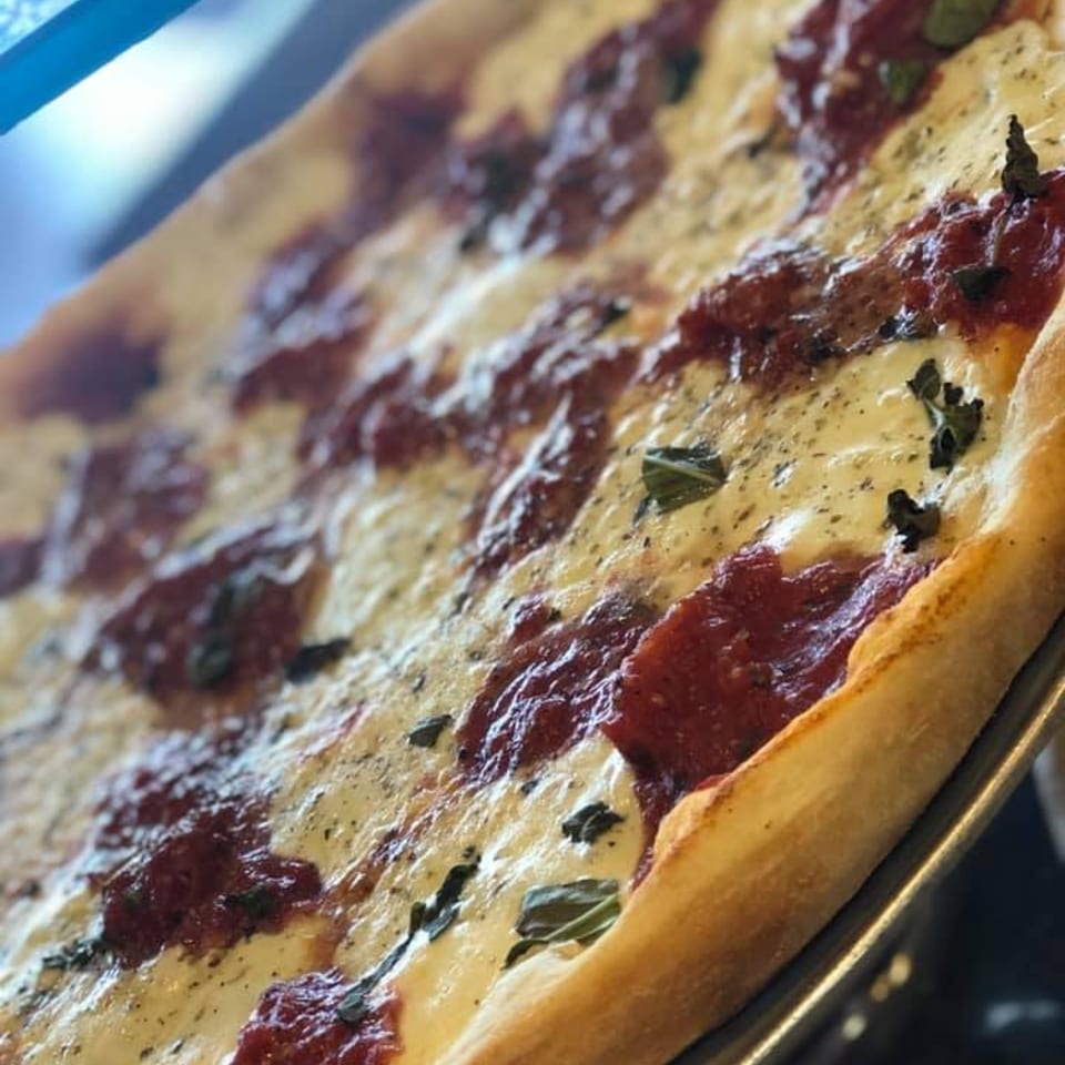 Close-up of a Pennachio's pizza with melted cheese, red sauce, and basil on a metal tray.
