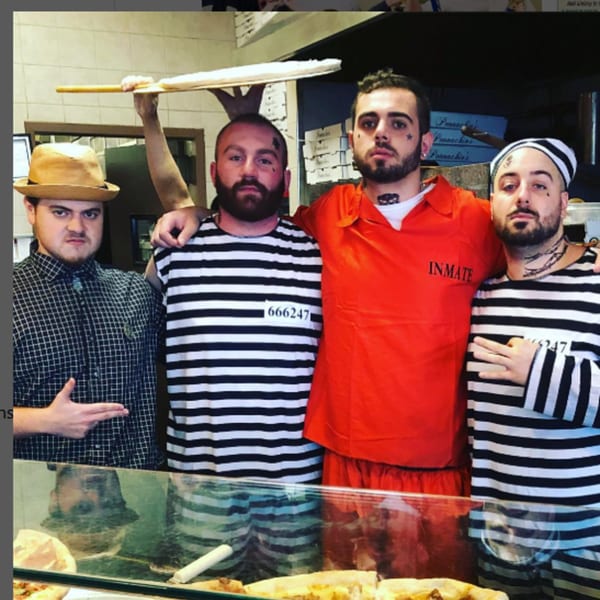 Four men in costume, two in striped prisoner outfits, one in an orange inmate uniform, and one in a fedora.