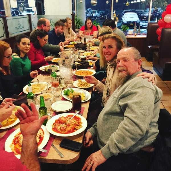 A large group of people enjoying pasta and drinks at a long table inside Pennachio's.