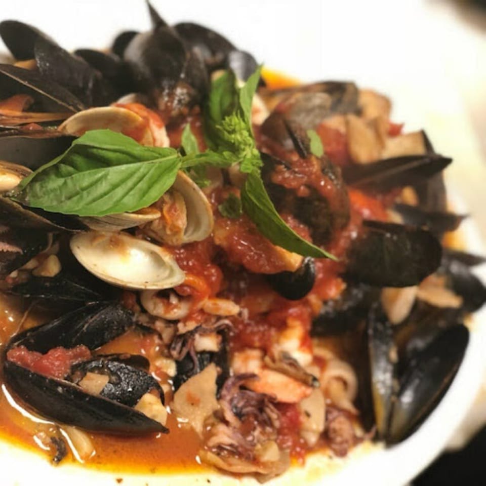 A close-up of Pennachio's seafood dish with mussels, clams, and squid in a rich red sauce, garnished with basil.