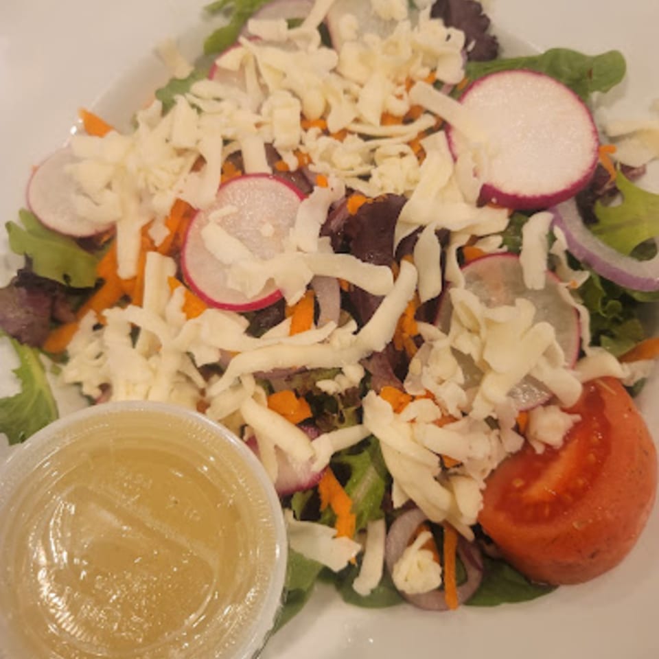 Pennachio's side salad with mixed greens, shredded cheese, radishes, carrots, red onion, and a side of dressing.