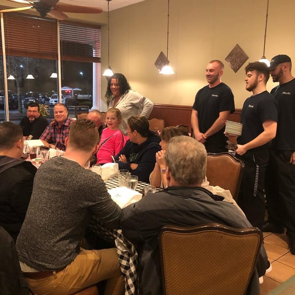 Pennachio's staff in black shirts standing behind a table of seated restaurant patrons.