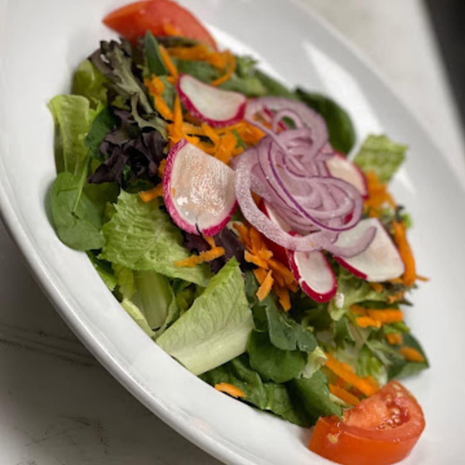 A fresh Pennachio's garden salad with mixed greens, red onion, radishes, carrots, and tomato.