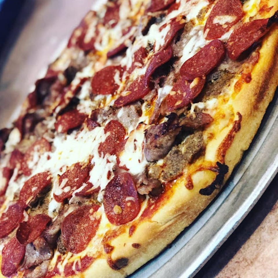 A Pennachio's pizza with pepperoni, sausage, and melted cheese on a golden crust.