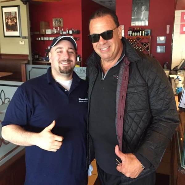 Two men, one in a Pennachio's shirt, smiling and giving thumbs up inside the restaurant.