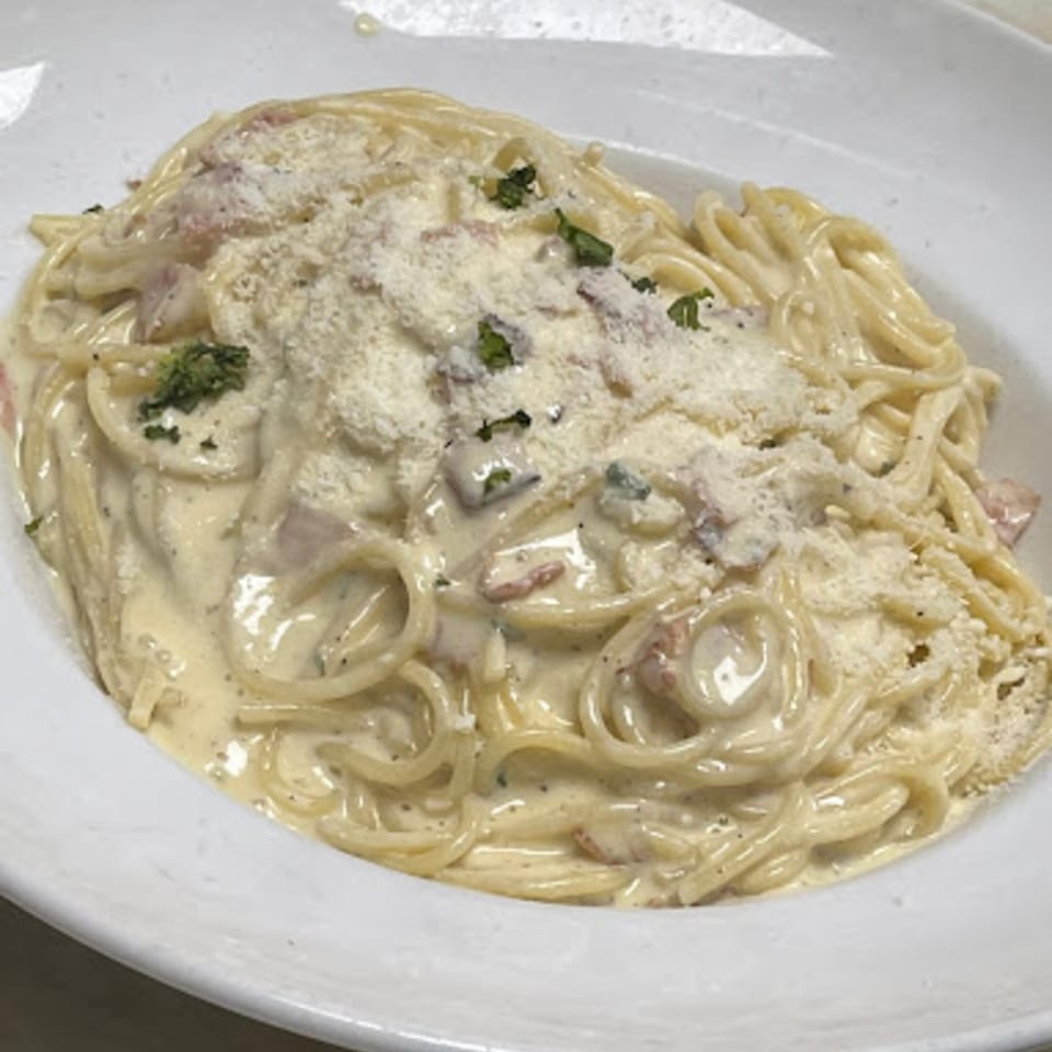 A white bowl filled with creamy spaghetti carbonara, topped with grated cheese and fresh herbs.